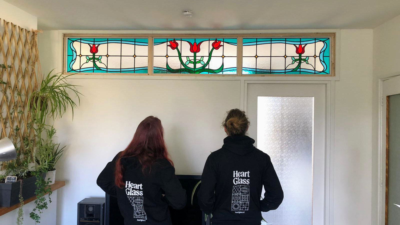 Twee medewerkers in Heart Glass hoodies bekijken een pas geplaatst bovenlicht met tulpen