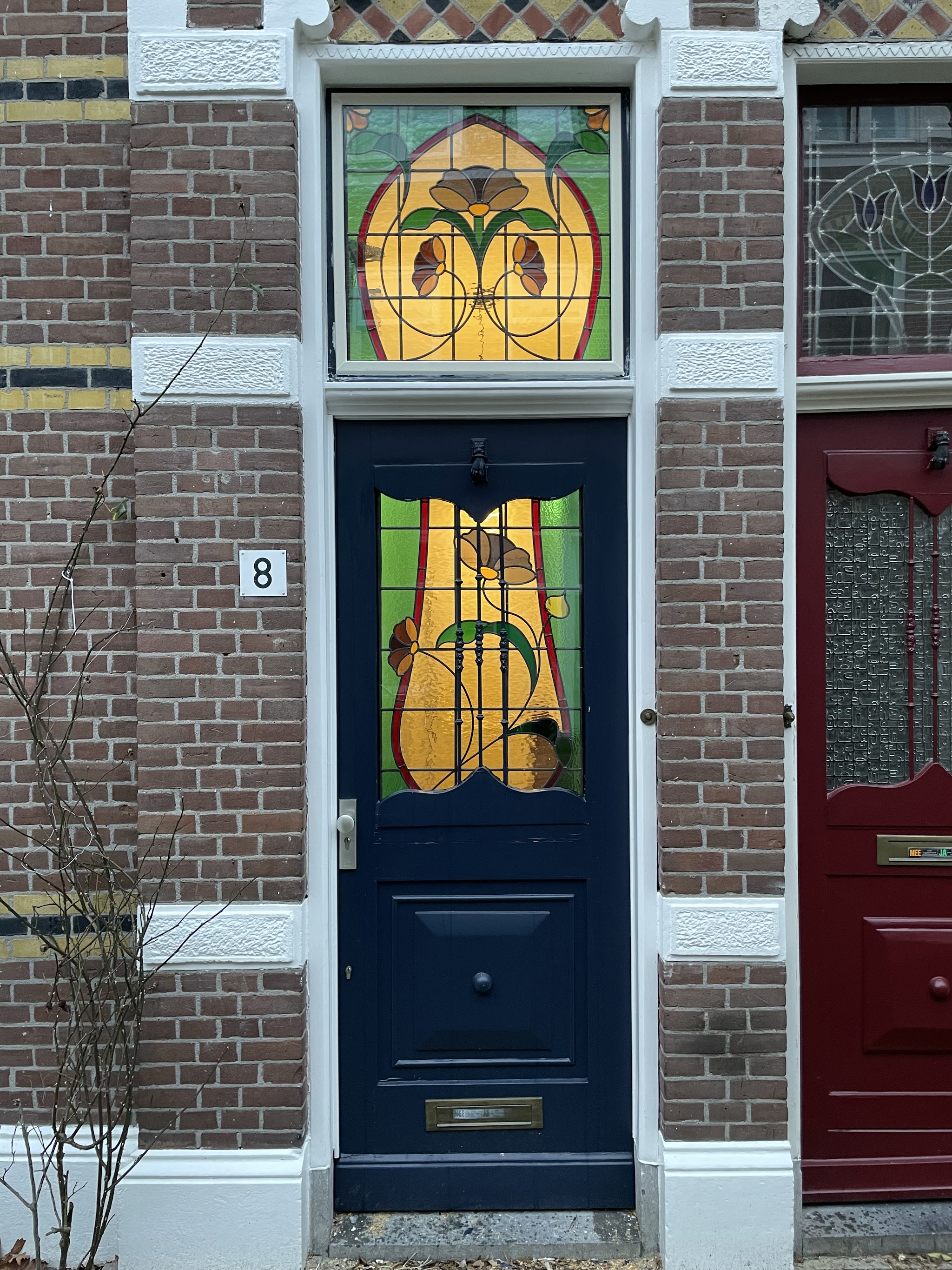 Donkerblauwe voordeur met glas-in-lood bovenlicht en deurpaneel in een bakstenen gevel