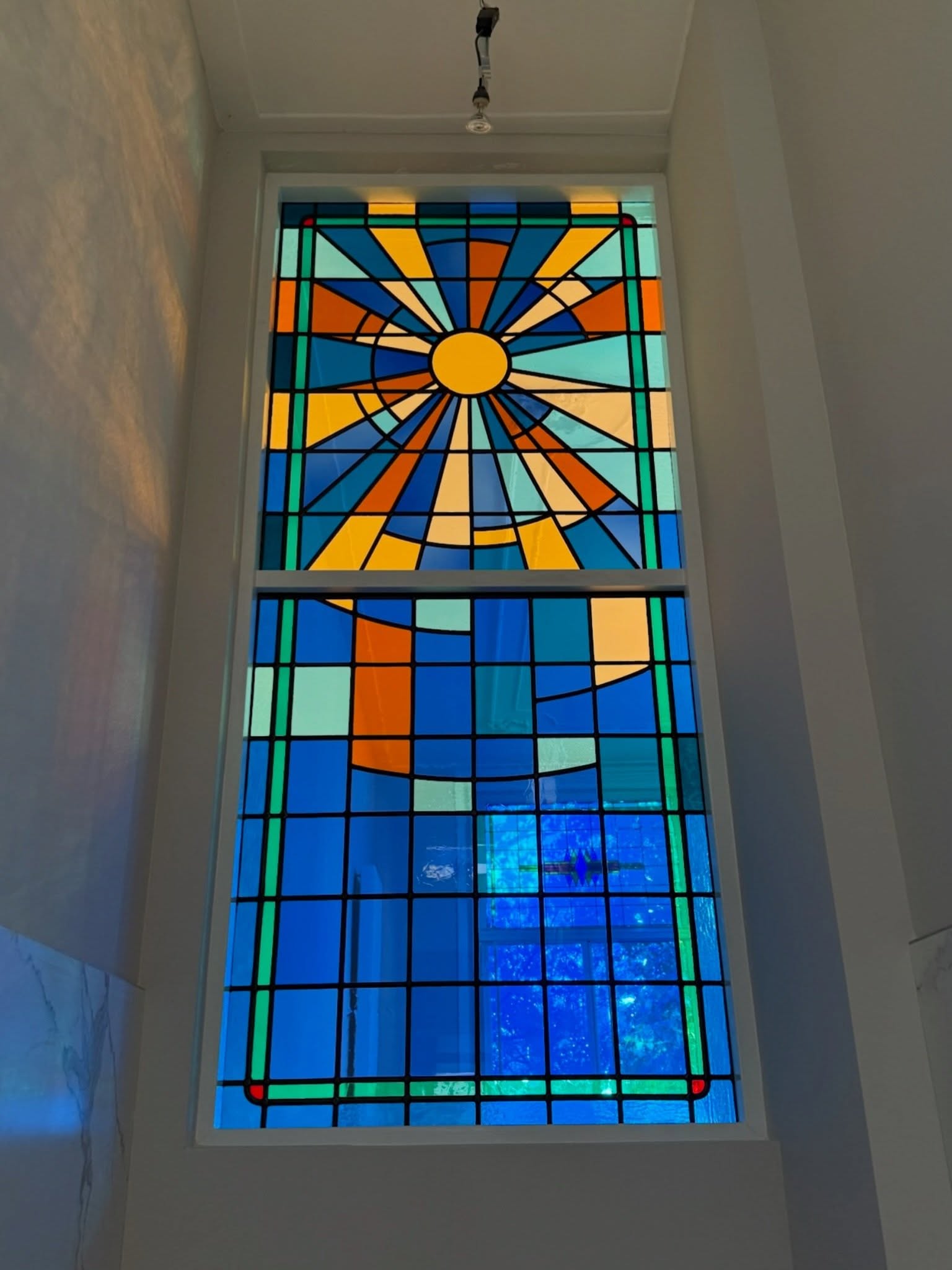 Hoog trappenhuisraam met zonnestralen in blauw en oranje glas